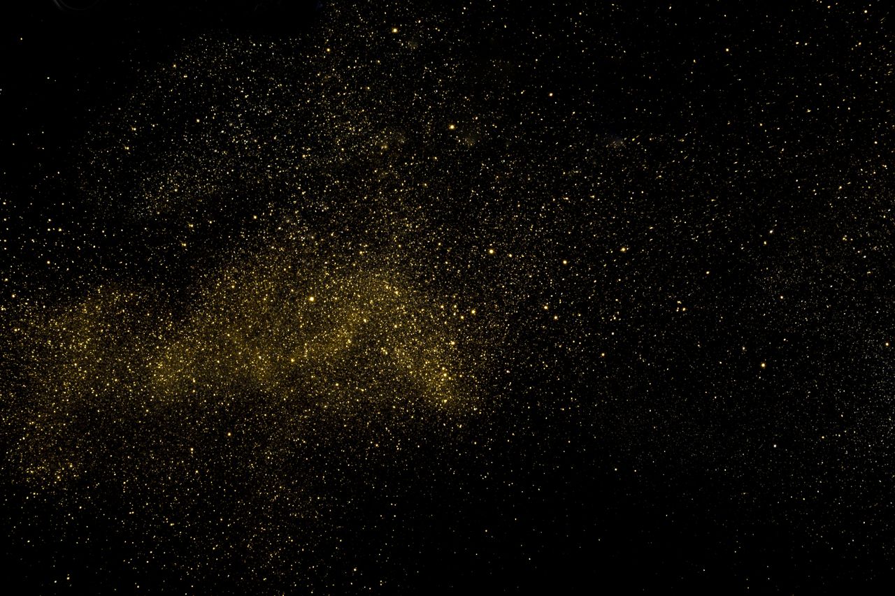 A captivating cosmic scene with golden dust resembling stars against a deep black background.
