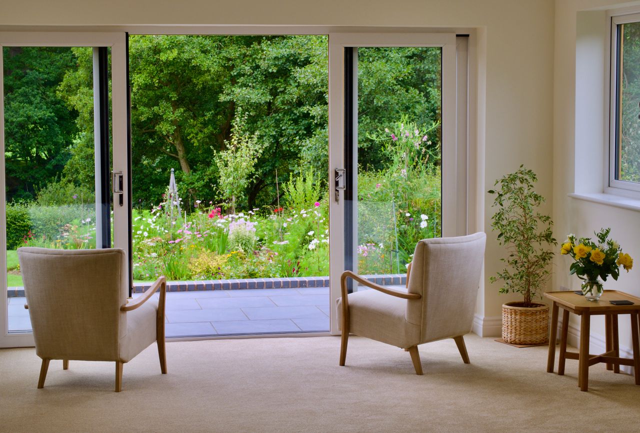 Cozy interior with armchairs and greenery view through large sliding glass doors.