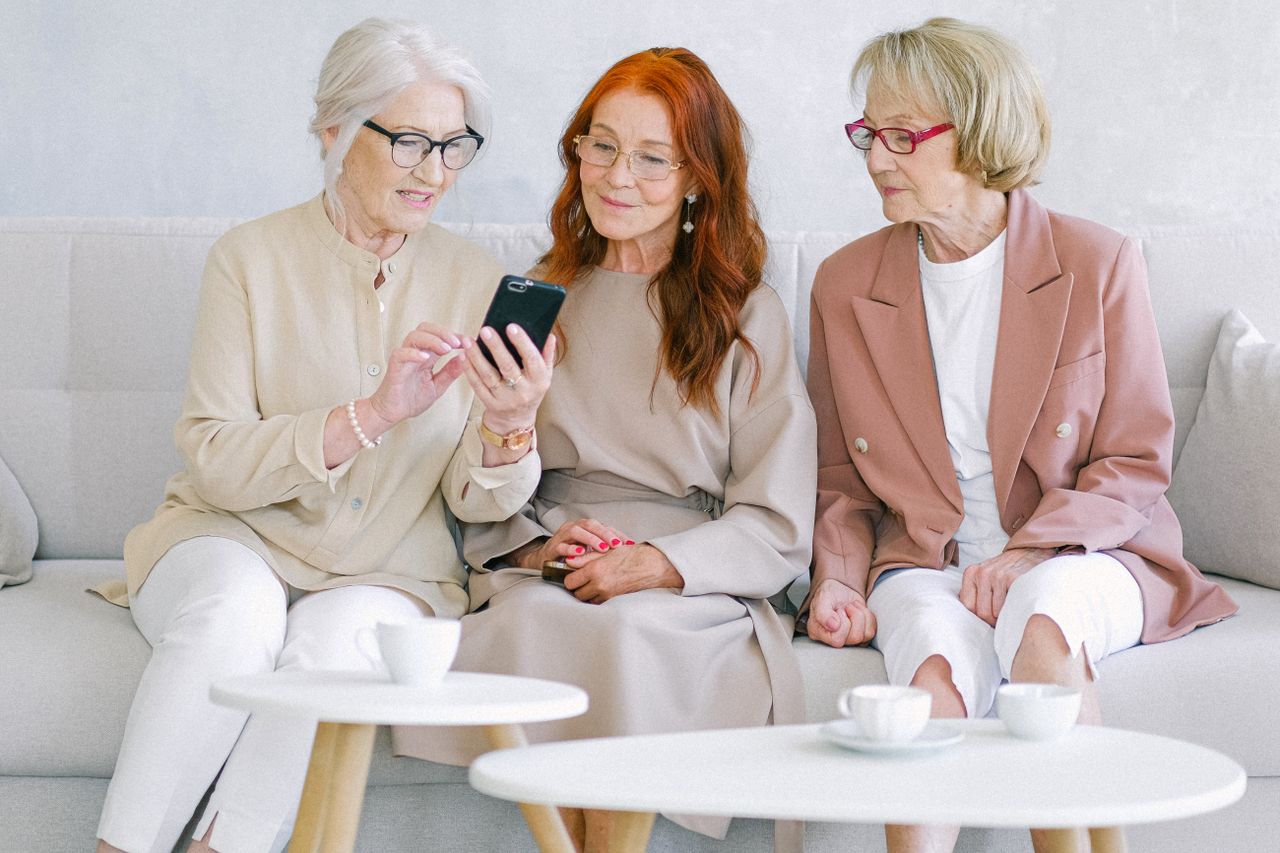 Three senior women sitting on a sofa, sharing a moment on a smartphone.